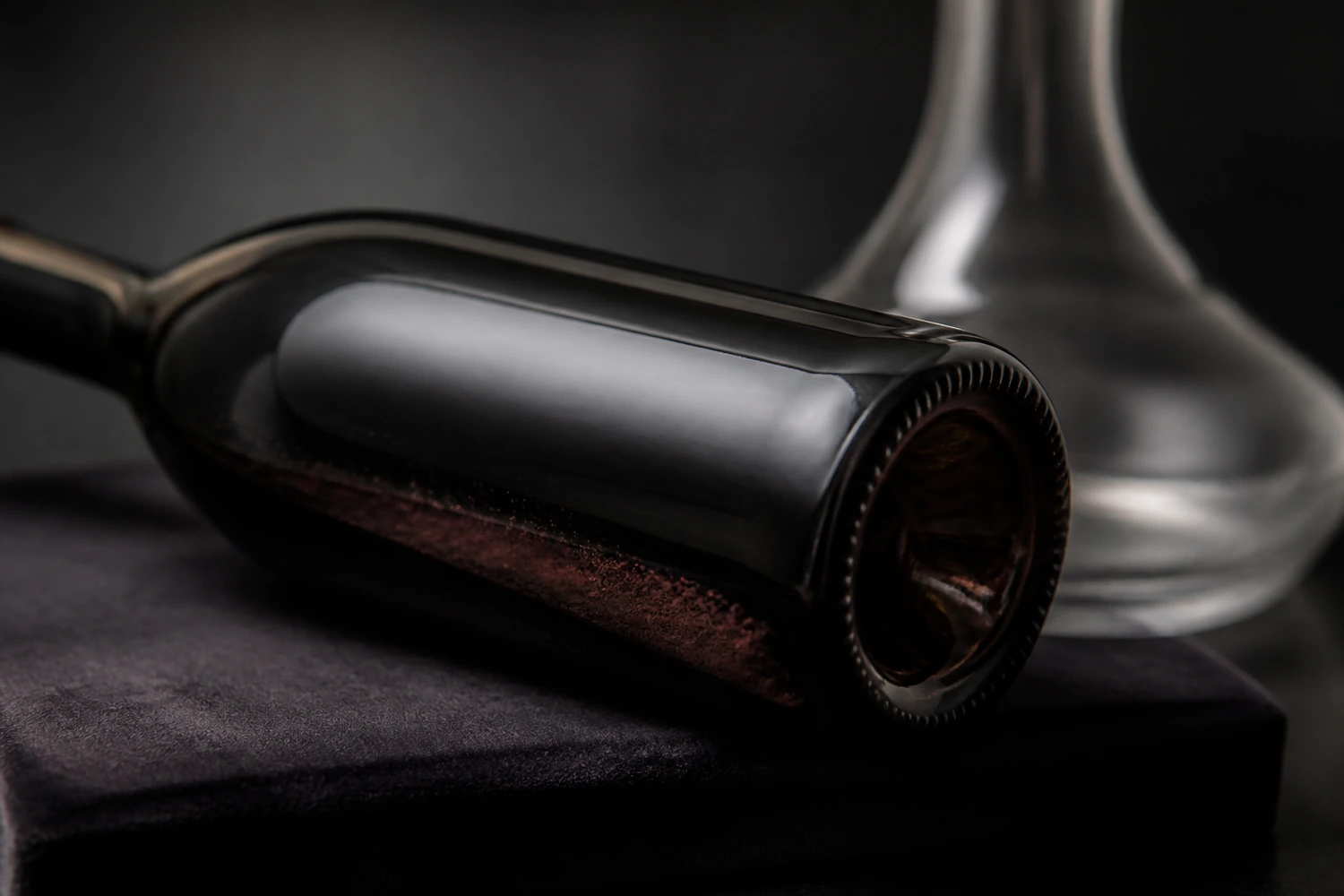 aged-red-wine-sediment-detail Fine natural red-brown sediment resting inside the shoulder of an unlabeled mature red-wine bottle beside a clear decanter.