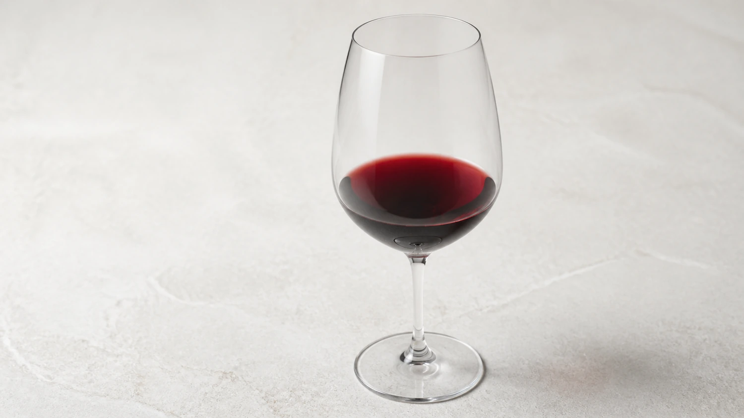how-to-read-red-wine-color A clear glass of red wine tilted over a neutral white tasting surface, revealing differences between its deep ruby core and lighter garnet rim.