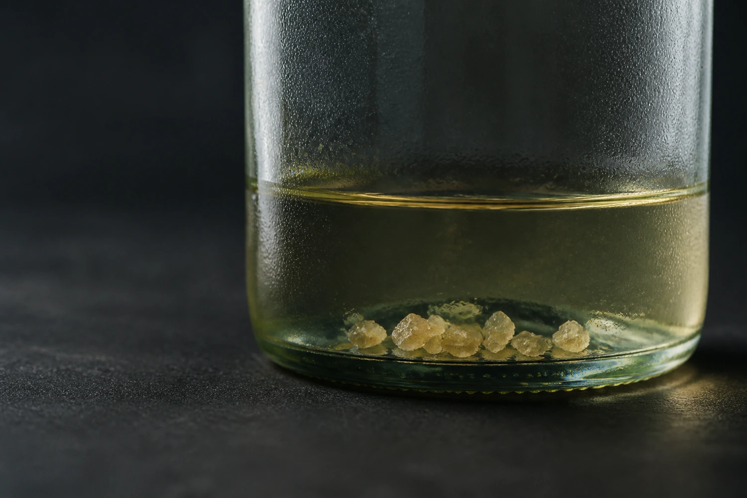 Natural tartrate crystals visible at the base of a chilled white-wine bottle, shown as harmless crystalline deposits rather than broken glass.